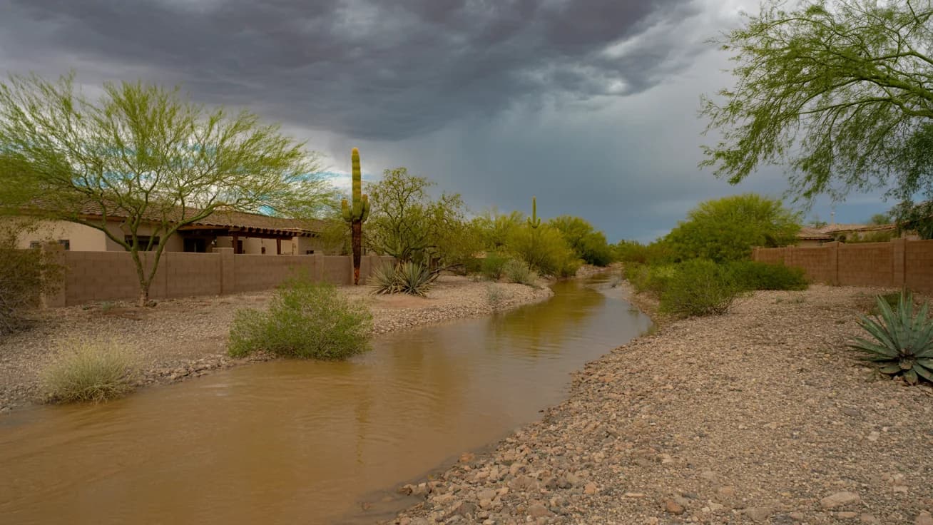 Arizona desert wash running with monsoon storm water near a residential neighborhood